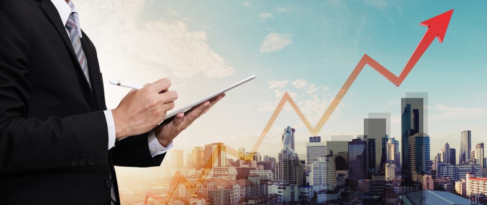 Businessman working on digital tablet, with panorama city view and raising up graph and arrow, representing business growth