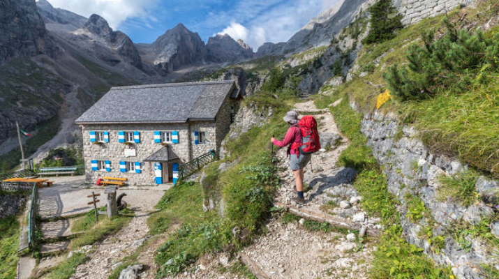 Hiker leaving the hut Onorio Falier at Pian di Ombretta, Ombretta valley, Marmolada, Dolomites, Belluno, Veneto, Italy