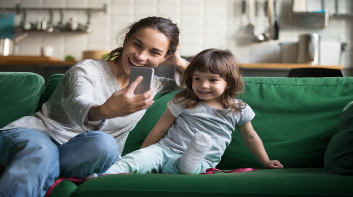 Happy mother laughing taking selfie with child daughter on smartphone at home, smiling single mom and cute girl playing making photo posing for self portrait, mommy and kid shooting instagram stories (Happy mother laughing taking selfie with child dau
