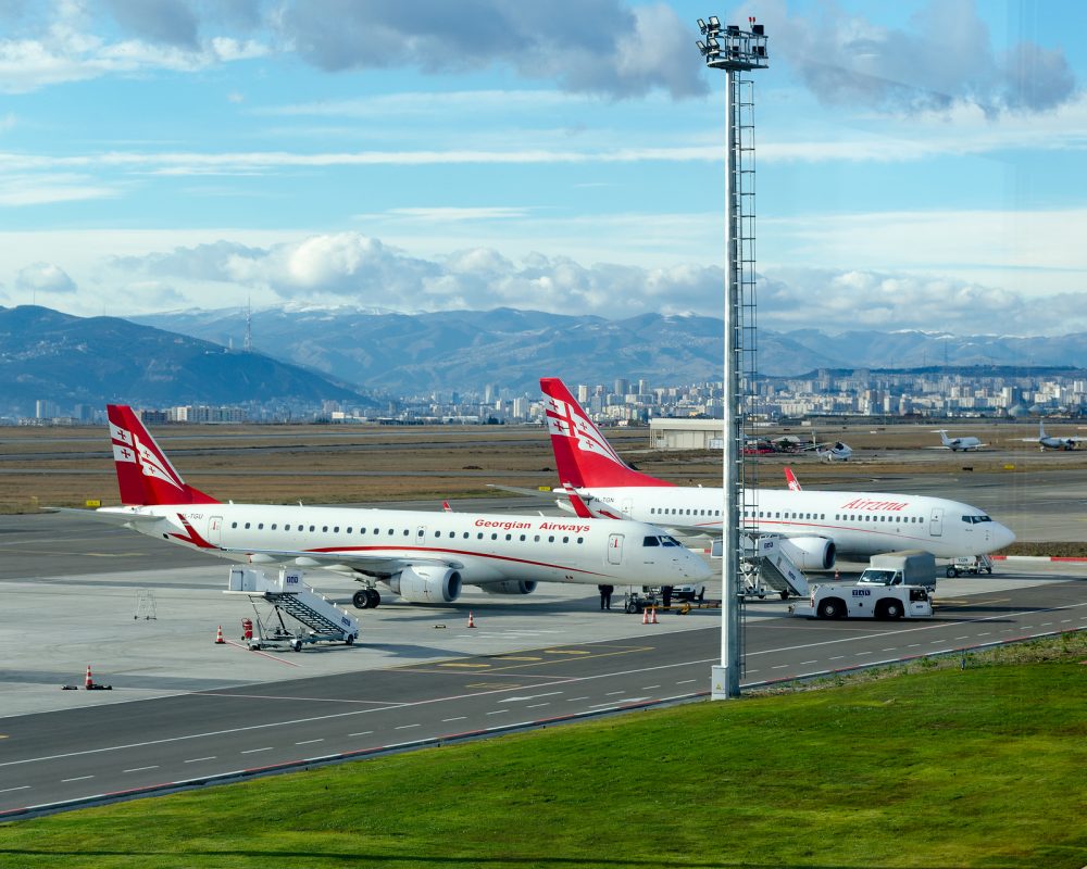 Tbilisi, Georgia, 12/07/2017: Two Georgian airplanes Airzena airways are parked at airport. In background beautiful landscape - city skyscrapers, mountains and sky with clouds.