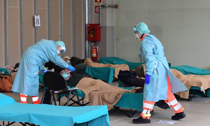 Hospital employees wearing a protection mask and gear tend to a patient (C) at a temporary emergency structure set up outside the accident and emergency department, where any new arrivals presenting suspect new coronavirus symptoms are being tested, at the Brescia hospital, Lombardy, on March 13, 2020. (Photo by Miguel MEDINA / AFP) (Photo by MIGUEL MEDINA/AFP via Getty Images)