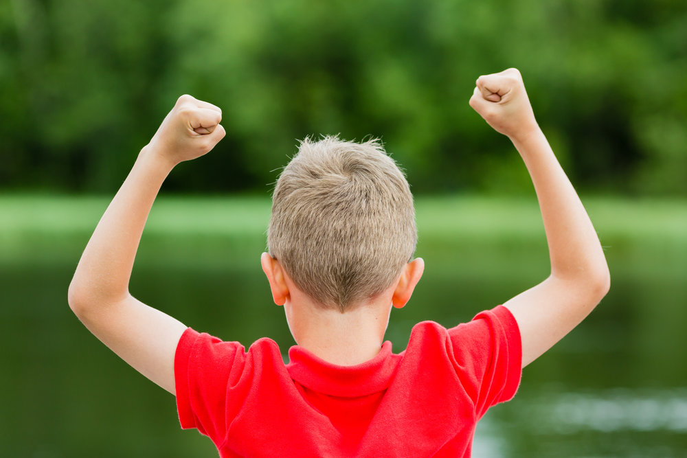 Boy with raised arms and fists in the air celebrating success or victory.