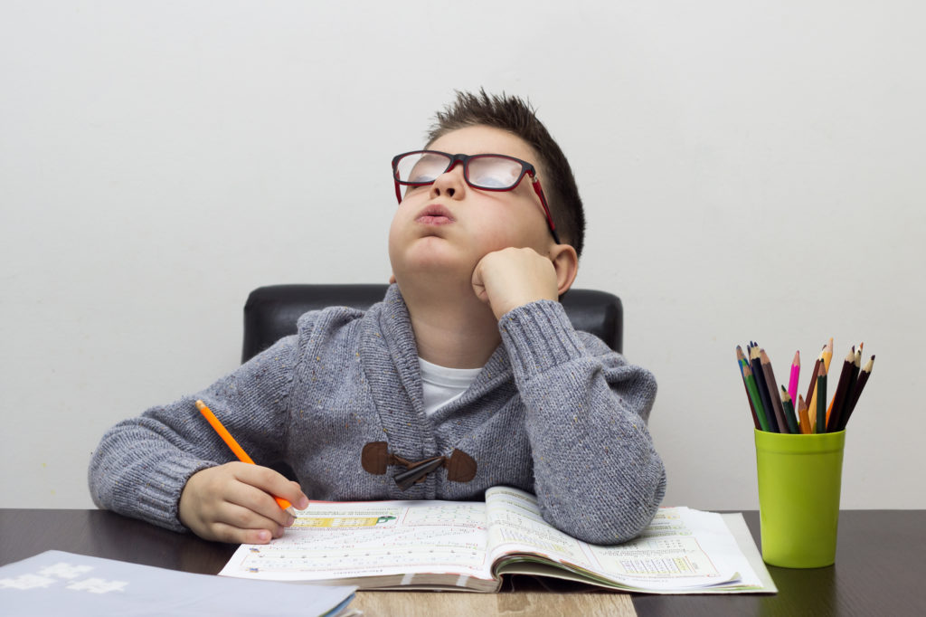 young boy frustrated over homework, writing at home. Boy studying at table. Kid drawing with a pencil.