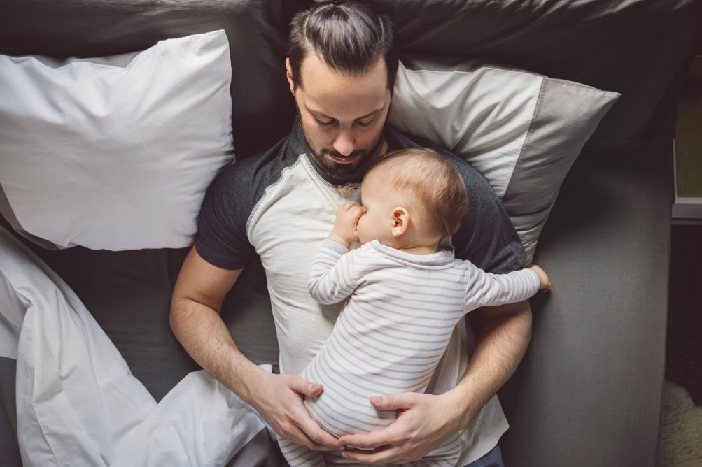 From above photo of handsome Caucasian man laying in bed with his baby.