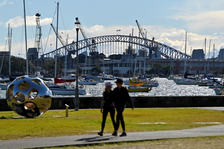 Residents walk in a park in front of the Harbour Bridge in Sydney on July 17, 2021, after authorities ordered new restrictions as a weeks-long lockdown failed to quash an outbreak of Covid-19. (Photo by Steven SAPHORE / AFP)
