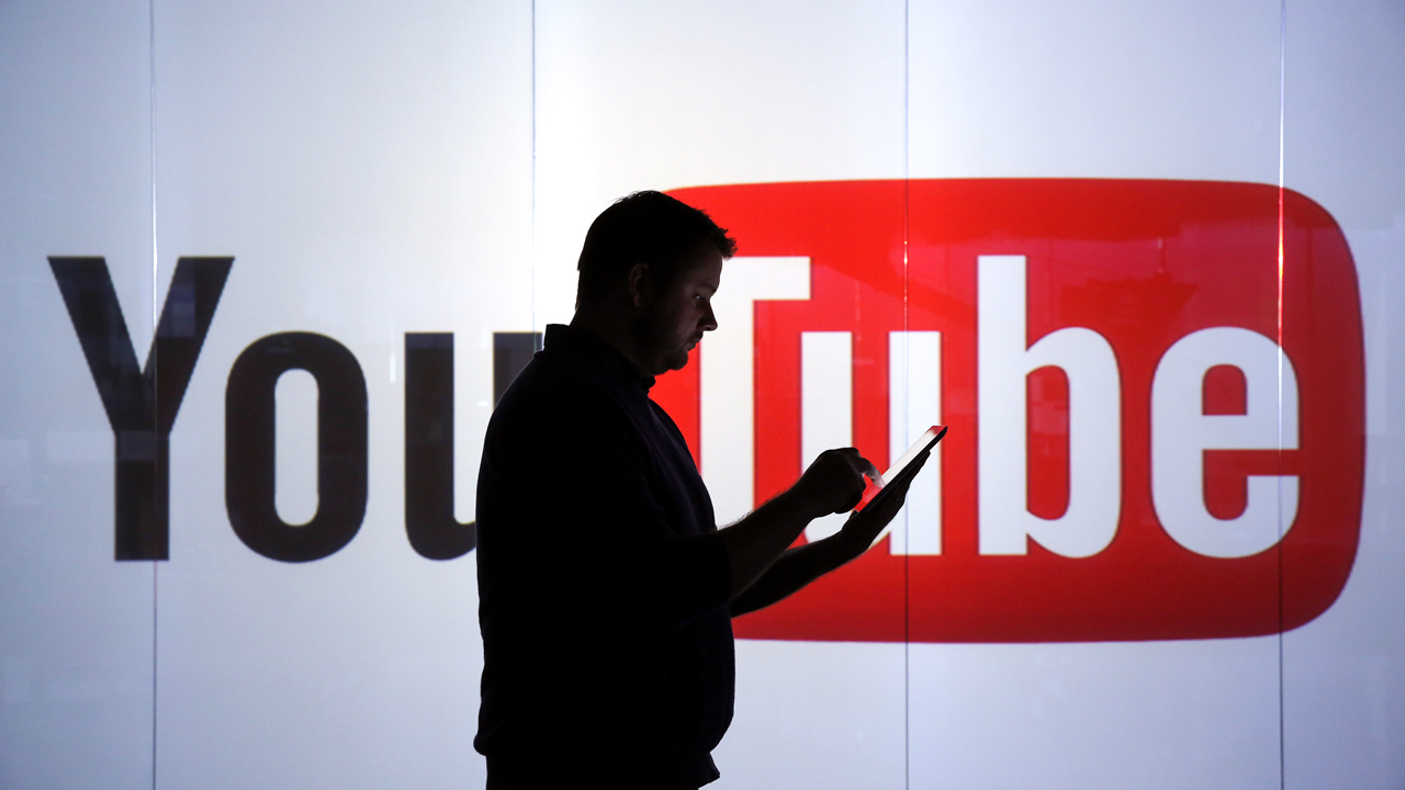 A man is seen as a silhouette as he checks a mobile device whilst standing against an illuminated wall bearing YouTube Inc.'s logo in this arranged photograph in London, U.K., on Tuesday, Jan. 5, 2016. YouTube Inc. provides consumer media and entertainment through its website. Photographer: Chris Ratcliffe/Bloomberg via Getty Images