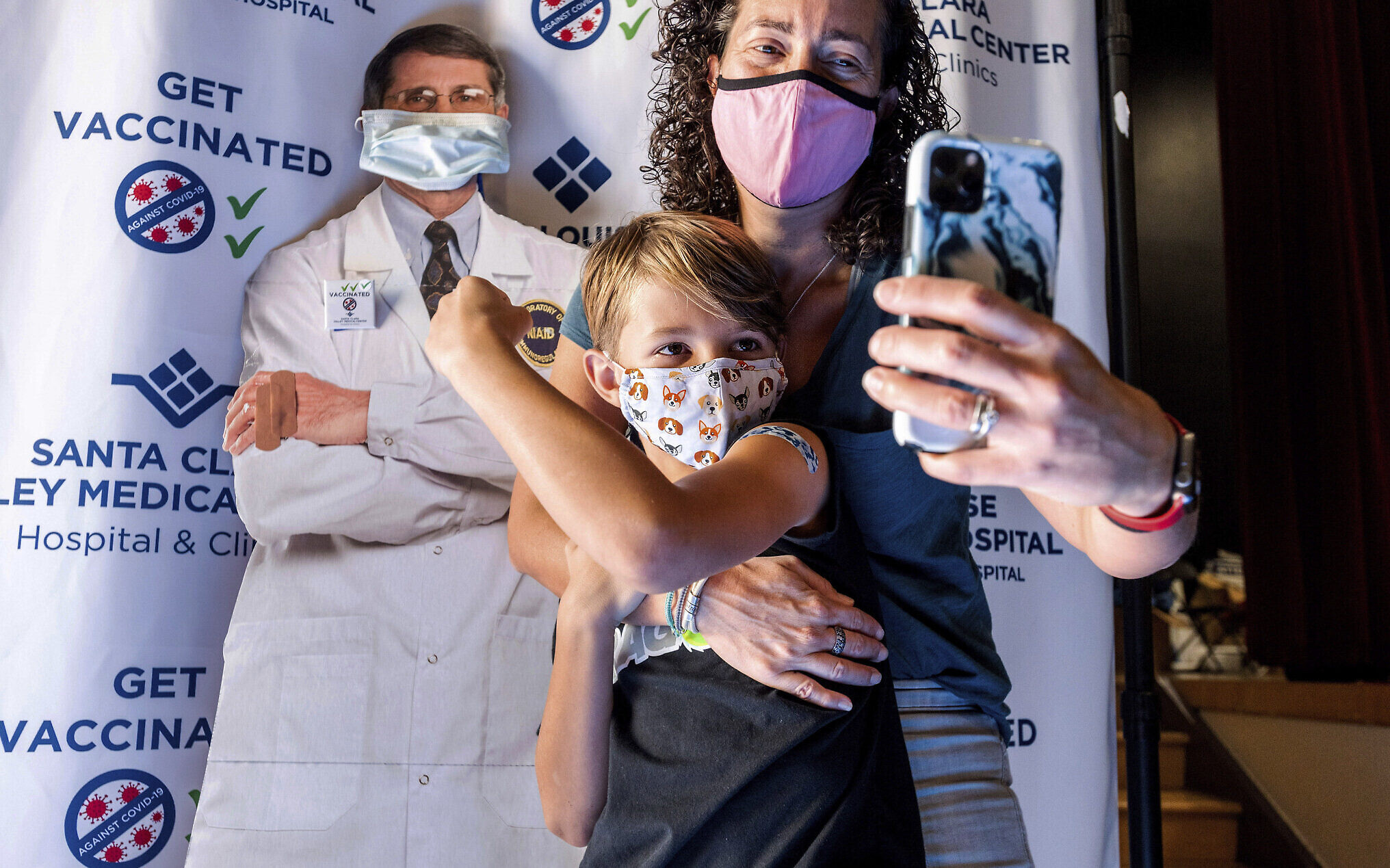 Finn Washburn, 9, poses for a photo with his mother, Kate Elsley, in front of a picture of Dr. Anthony Fauci after he received a Pfizer COVID-19 vaccine in San Jose, Calif., Wednesday, Nov. 3, 2021. The U.S. entered a new phase Wednesday in its COVID-19 vaccination campaign, with shots now available to millions of elementary-age children. (AP Photo/Noah Berger)