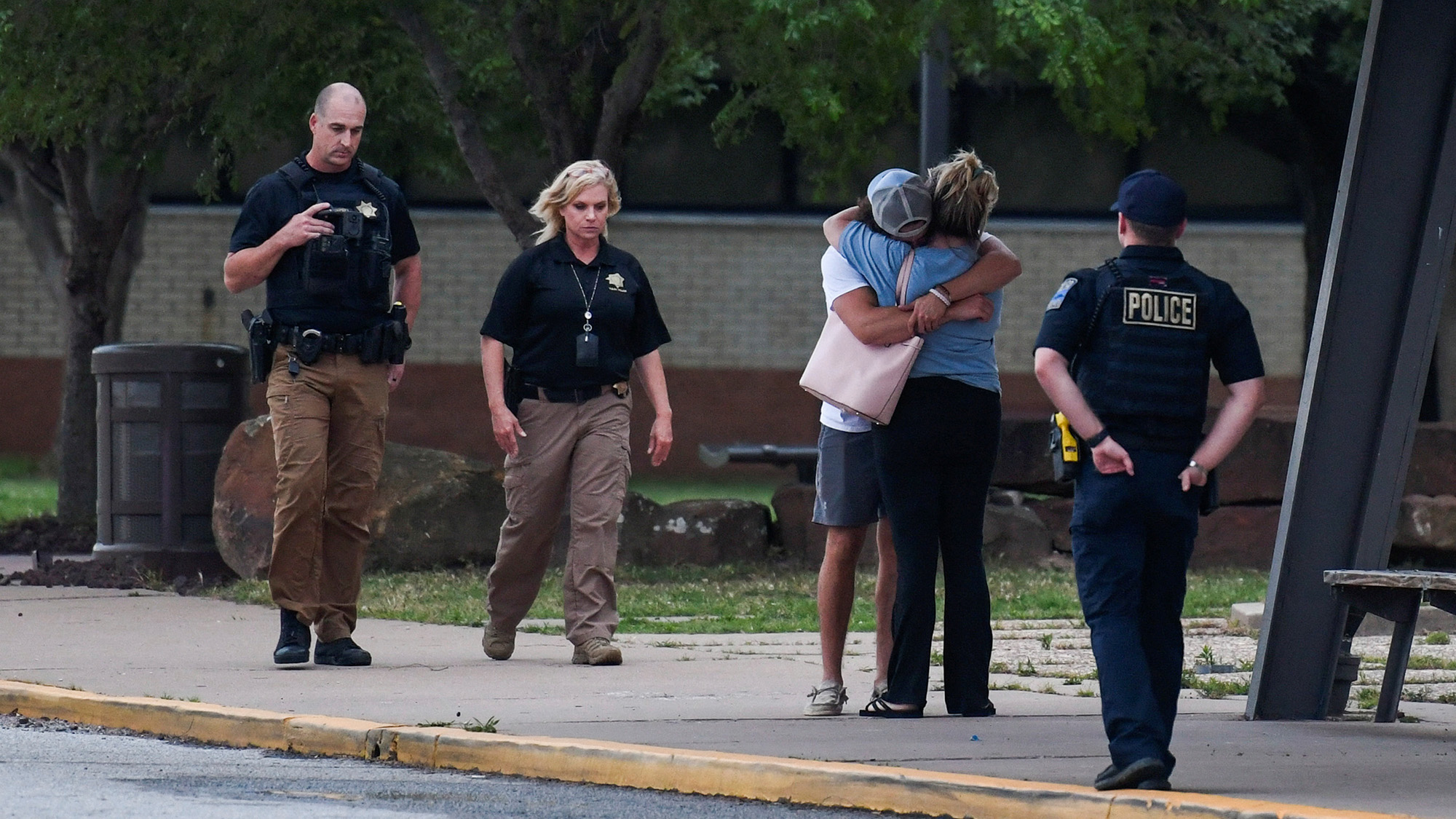 Police officers walk near people embracing at the reunion location, Memorial High School, where they wait to get more information after a shooting at the Saint Francis hospital campus, in Tulsa, Oklahoma, June 1, 2022.   REUTERS/Michael Noble Jr.