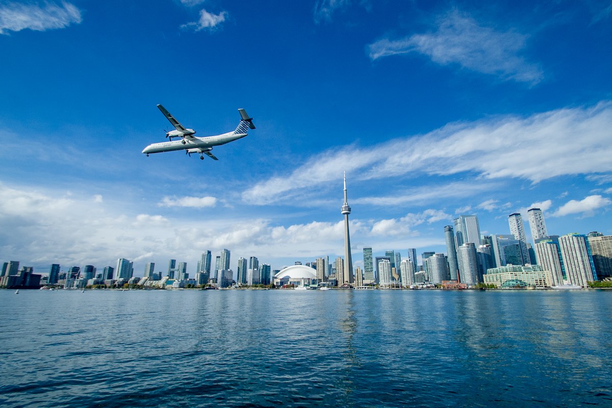 A propeller plane is preparing for landing in Billy Bishop airport (YTZ) and flying in front of Toronto's waterfront, as seen from Lake Ontario