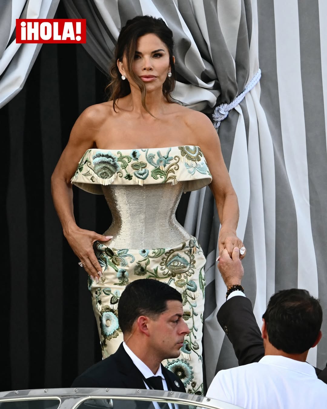 Lauren Sánchez lució un vestido de escote palabra de honor y silueta de corset en color verde metálico con bordados florales; mientras que Jeff llevó un traje marrón con camisa blanca sin corbata para dirigirse a The Madonna C